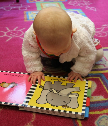 Baby looking at a book on a pink carpet