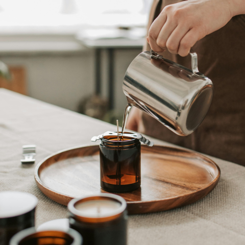 Woman pouring liquid wax into jar to make candle.