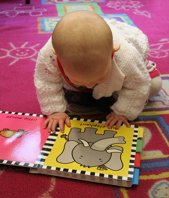 Baby reading a book on a pink carpet