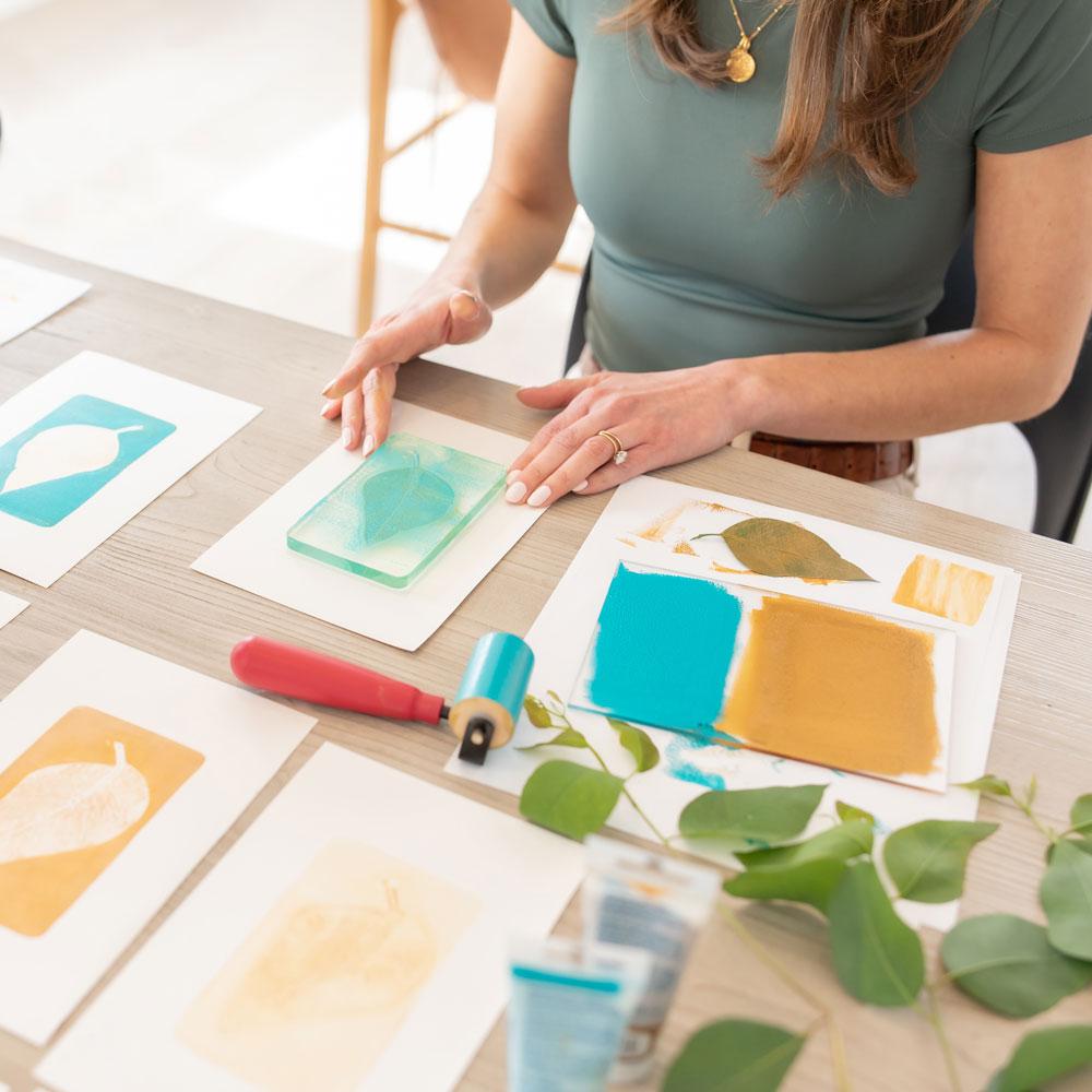 woman using gel plate to print art of leaves